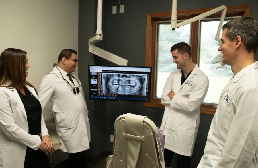 Four Harrison Dental Group dentists talking together beside an x-ray on a monitor.